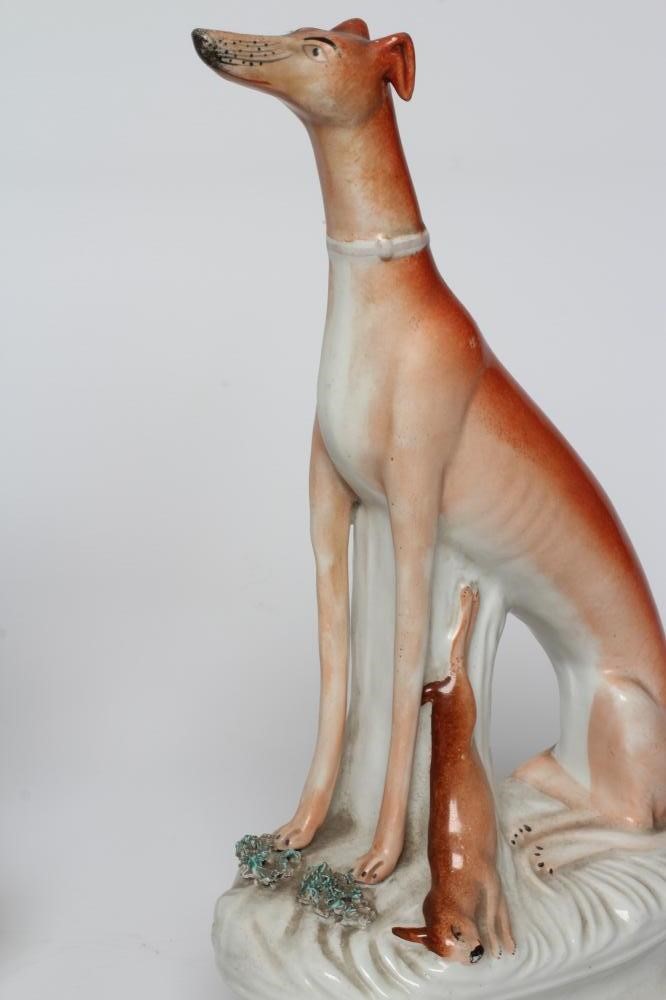 A PAIR OF VICTORIAN STAFFORDSHIRE POTTERY GREYHOUNDS modelled seated with free-standing fore-legs Image