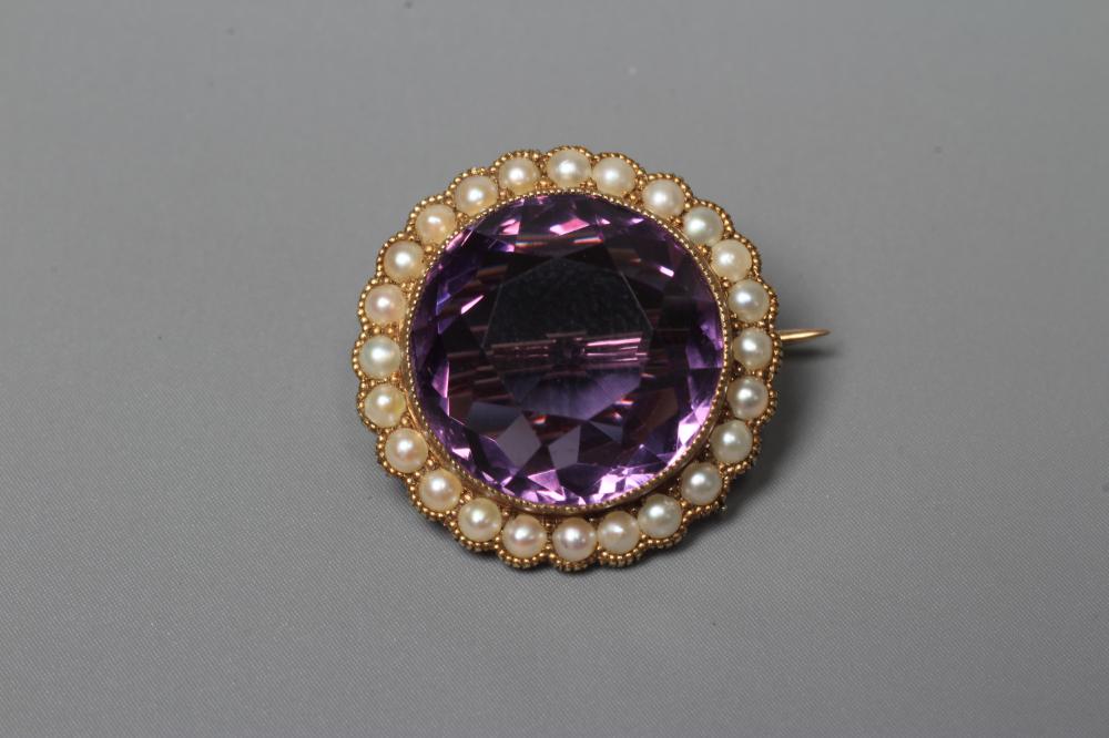 AN EDWARDIAN AMETHYST AND SEED PEARL BROOCH, the circular facet cut amethyst collet set to a border Image