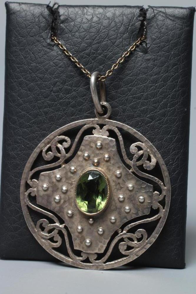 AN ARTS AND CRAFTS CIRCULAR PEWTER PENDANT, centred by an oval facet cut green stone in a planished Image