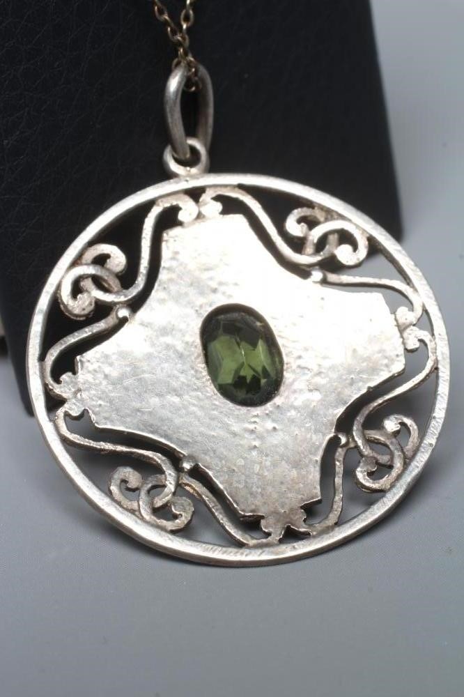 AN ARTS AND CRAFTS CIRCULAR PEWTER PENDANT, centred by an oval facet cut green stone in a planished Image