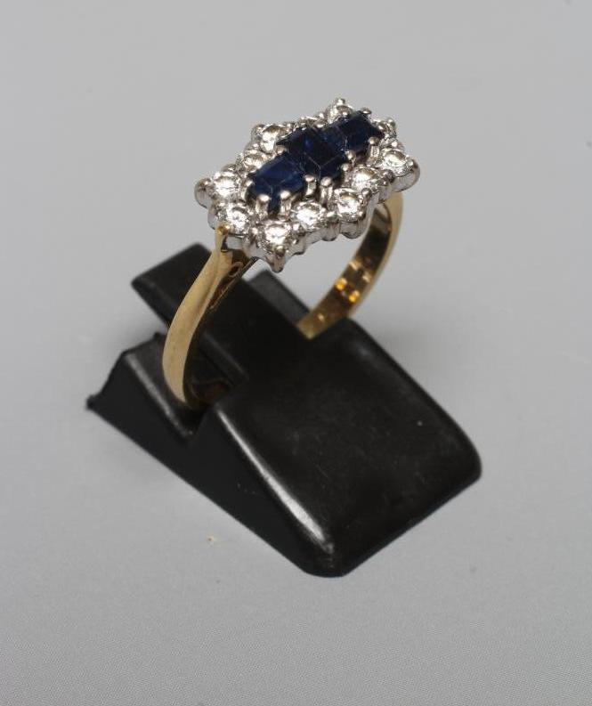 A SAPPHIRE AND DIAMOND RING, the three emerald cut sapphires claw set to a border of twelve Image