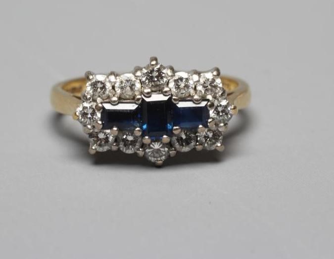 A SAPPHIRE AND DIAMOND RING, the three emerald cut sapphires claw set to a border of twelve Image
