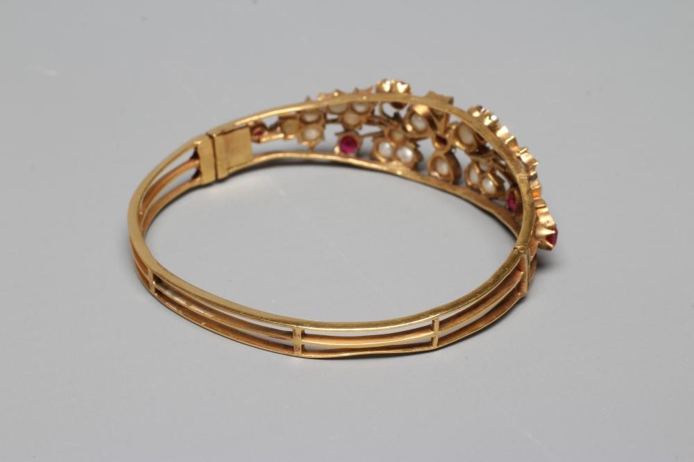 A LATE VICTORIAN STIFF HINGED BANGLE, the open upper section set with seven rubies and numerous Image