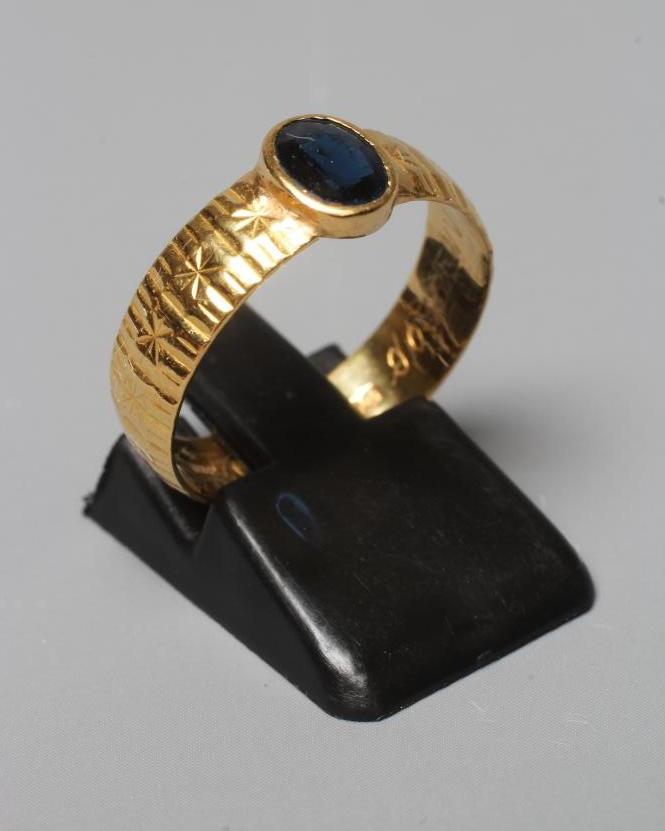 A SOLITAIRE SAPPHIRE RING, the oval facet cut stone in rub-over setting to a star and line cut 22ct Image