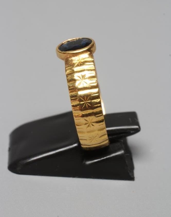 A SOLITAIRE SAPPHIRE RING, the oval facet cut stone in rub-over setting to a star and line cut 22ct Image