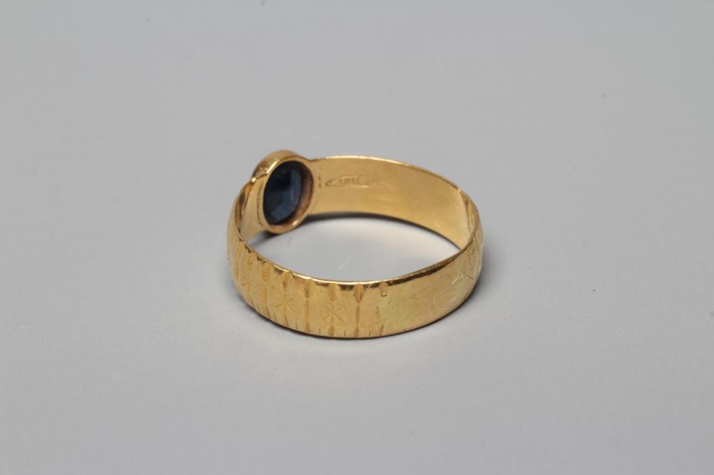 A SOLITAIRE SAPPHIRE RING, the oval facet cut stone in rub-over setting to a star and line cut 22ct Image