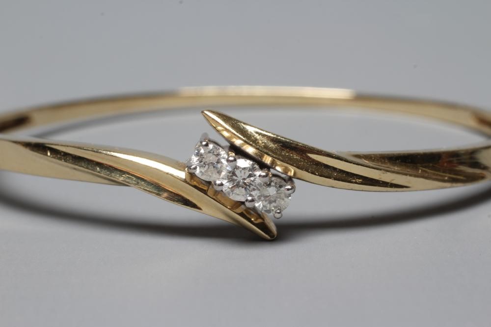 A DIAMOND STIFF HINGED BANGLE, the upper section with three brilliant cut stones in an open Image