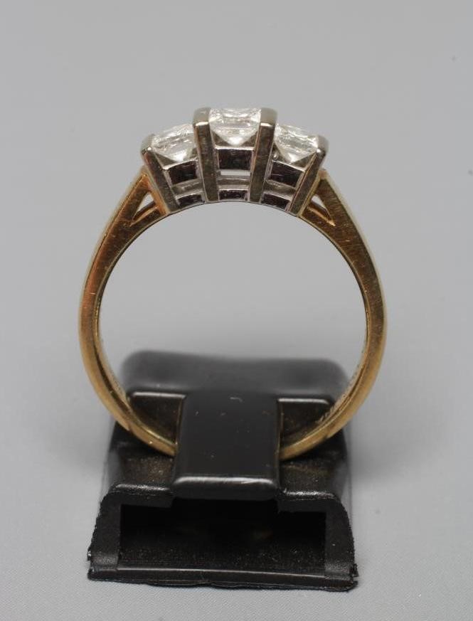 A THREE STONE DIAMOND RING, the Princess cut stones bar set to a plain shank, stamped 18K CORONA, Image