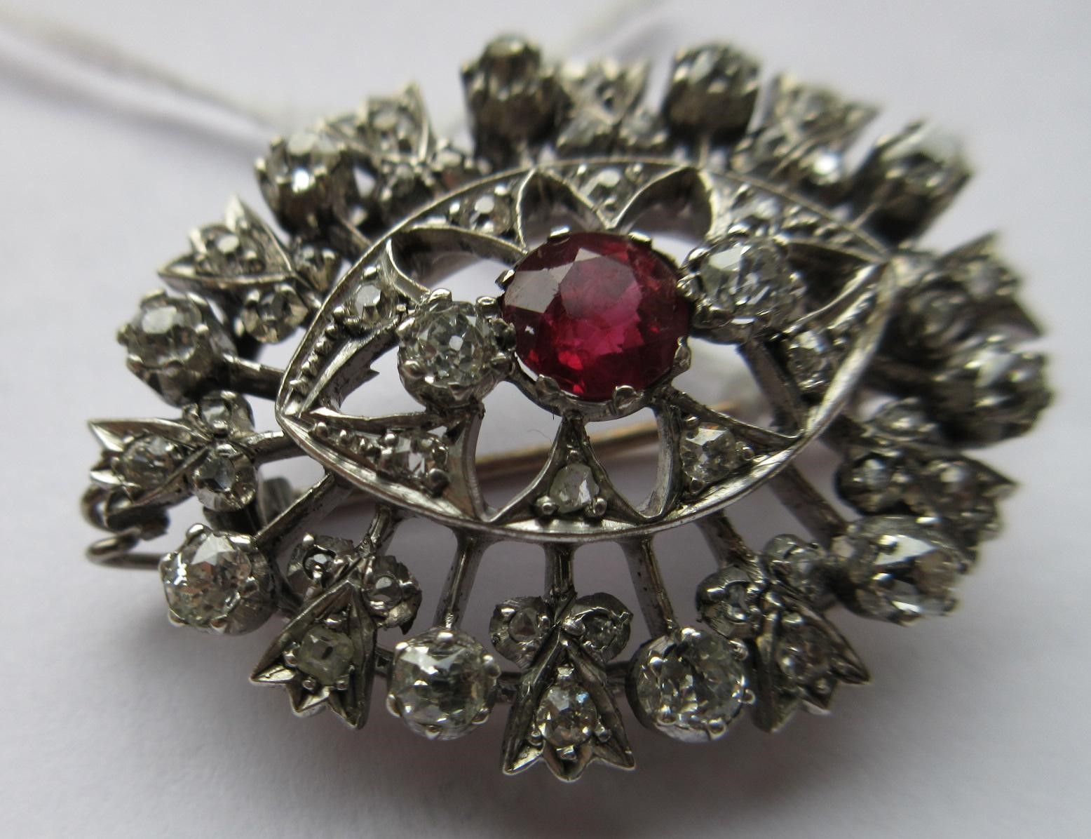 A RUBY AND DIAMOND BROOCH, the central circular facet cut ruby claw set to open borders of old mix Image
