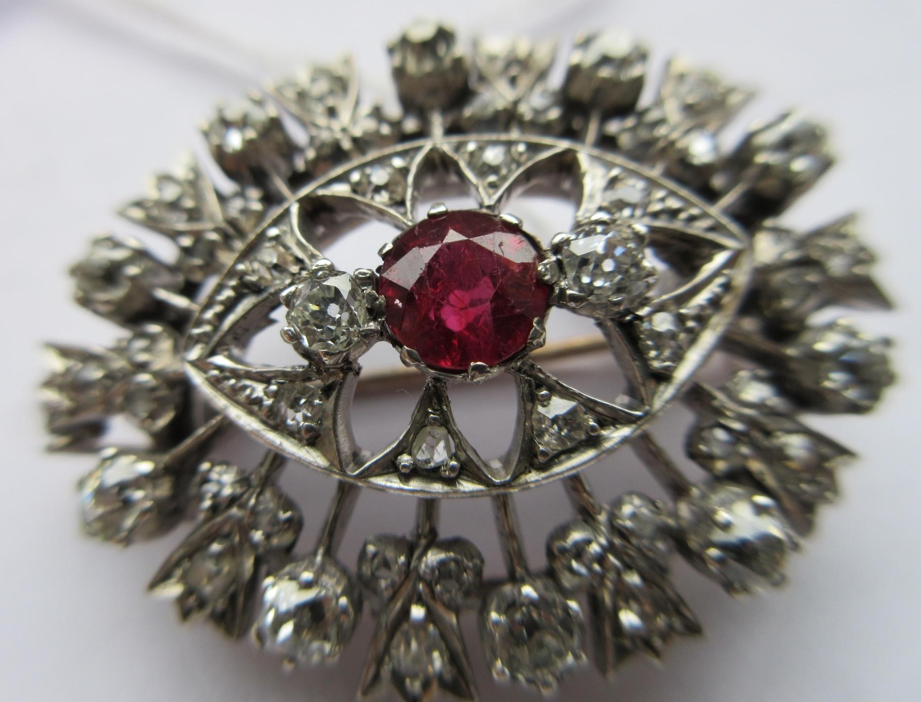 A RUBY AND DIAMOND BROOCH, the central circular facet cut ruby claw set to open borders of old mix Image