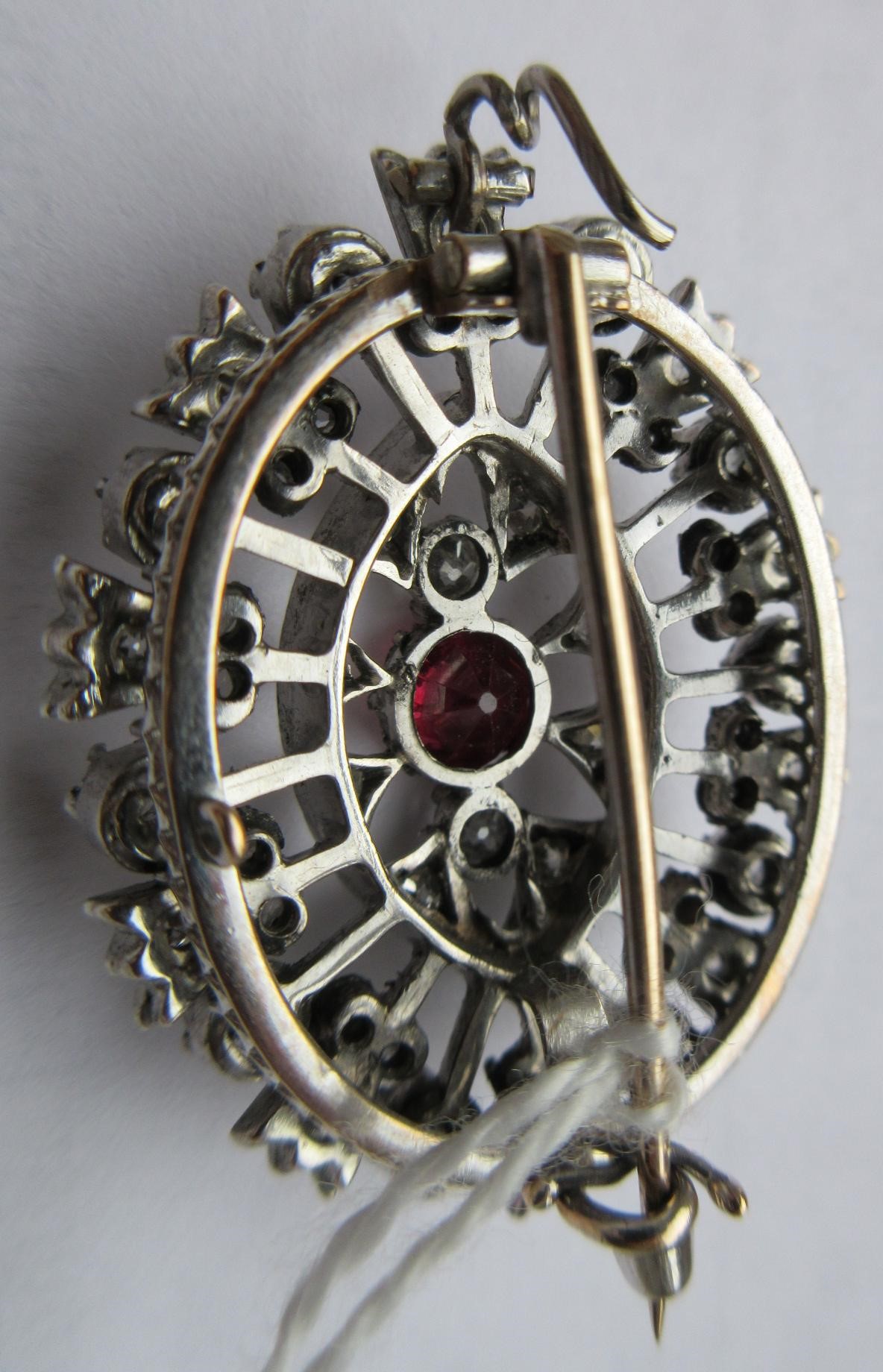 A RUBY AND DIAMOND BROOCH, the central circular facet cut ruby claw set to open borders of old mix Image