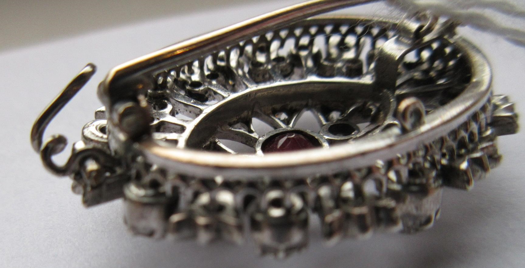 A RUBY AND DIAMOND BROOCH, the central circular facet cut ruby claw set to open borders of old mix Image