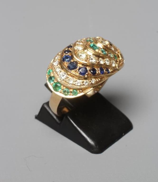 A MULTI-GEM COCKTAIL RING, the oval panelled boss set with rows of diamonds, emeralds and sapphires Image