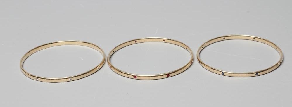 A MATCHED SET OF THREE STONE SET 9CT GOLD BANGLES Image