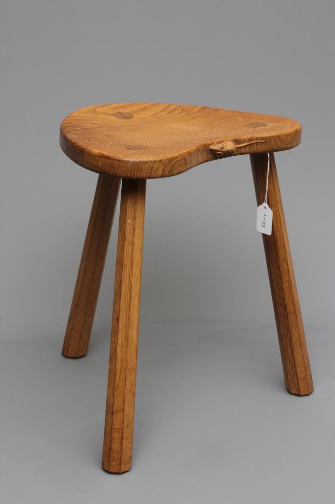 A ROBERT THOMPSON ADZED OAK COW STOOL, the dished kidney shaped top raised on three faceted splayed Image