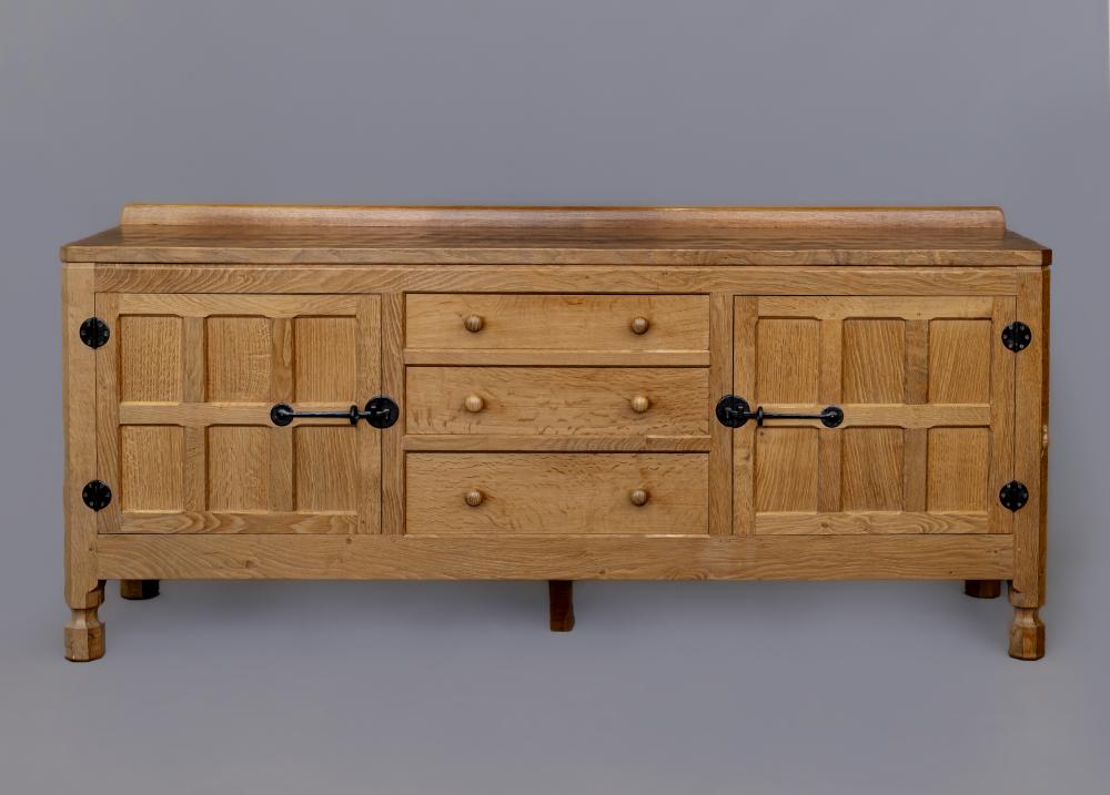 A ROBERT THOMPSON ADZED OAK SIDEBOARD of canted oblong form with ledge back Image