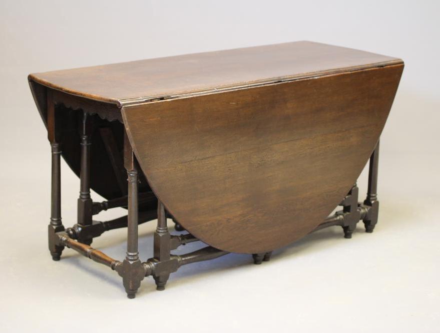 AN OAK GATELEG DINING TABLE, early 18th century, the boarded top raised on columnar legs joined by Image