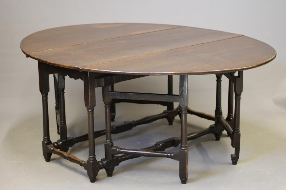 AN OAK GATELEG DINING TABLE, early 18th century, the boarded top raised on columnar legs joined by Image