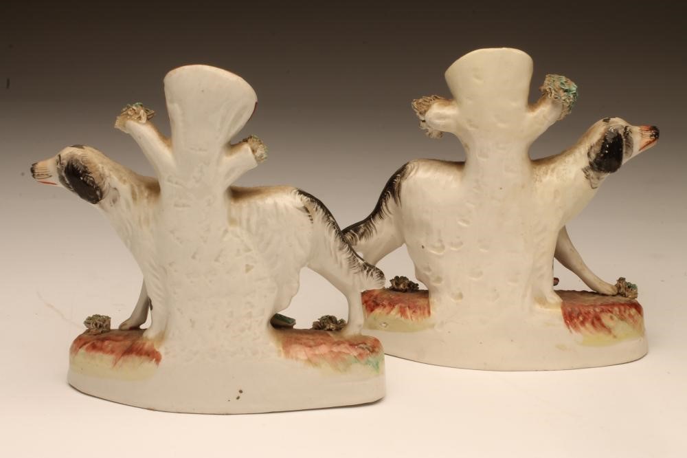 A PAIR OF VICTORIAN STAFFORDSHIRE POTTERY SPILL VASES as black and white retrievers standing against Image