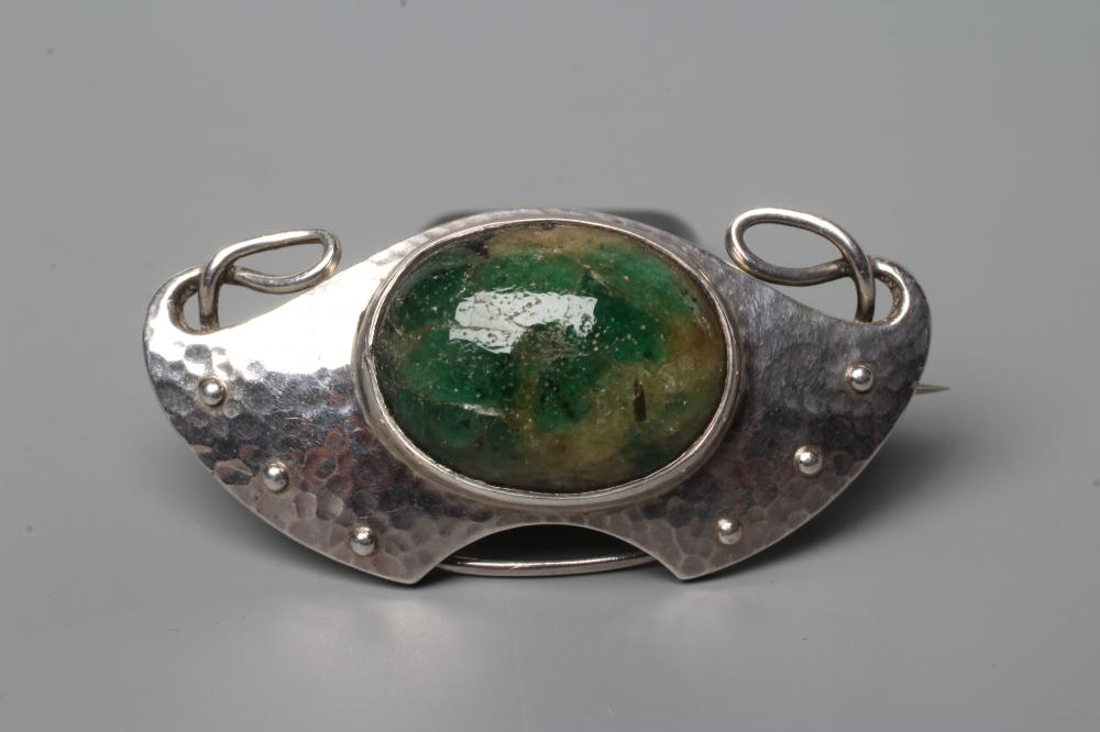 A MURRLE BENNETT BROOCH, the shaded green glass oval cabochon in a planished whiplash and wing Image