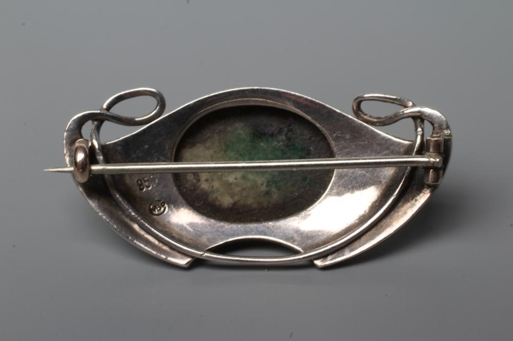 A MURRLE BENNETT BROOCH, the shaded green glass oval cabochon in a planished whiplash and wing Image