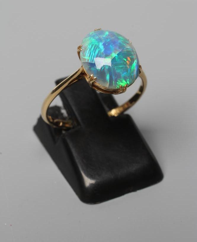 T. GAUNT - a black opal ring, the oval cabochon polished stone claw set to a plain shank, stamped Image