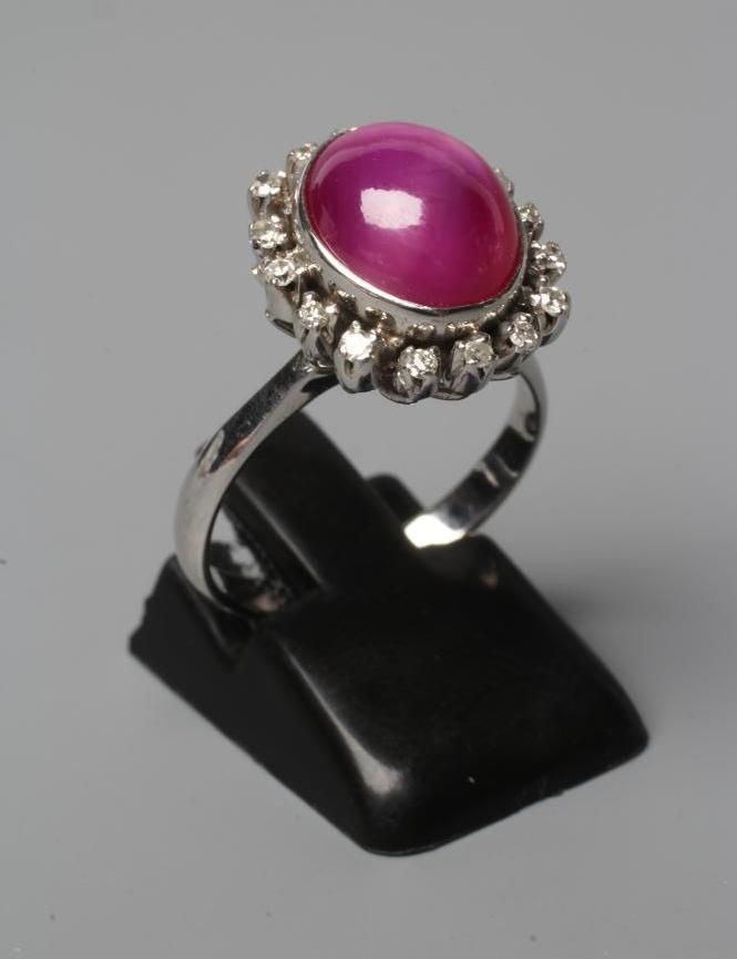 A STAR RUBY AND DIAMOND RING, the oval cabochon ruby collet set to a border of sixteen small Image