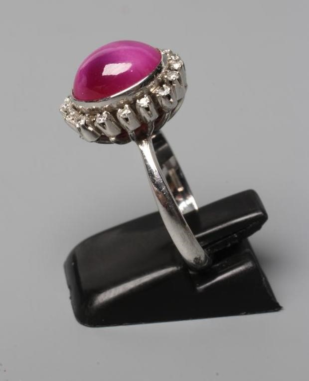 A STAR RUBY AND DIAMOND RING, the oval cabochon ruby collet set to a border of sixteen small Image