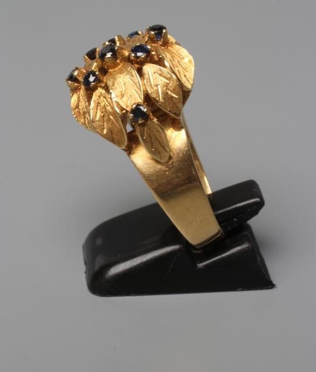 A COCKTAIL RING, the high flowerhead panel claw set with nine small sapphires to a plain wide shank Image