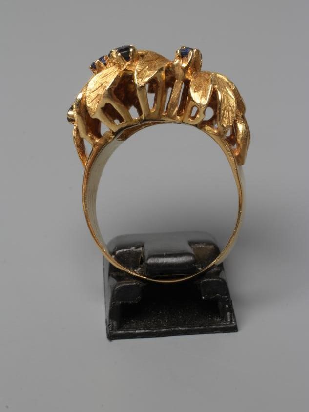 A COCKTAIL RING, the high flowerhead panel claw set with nine small sapphires to a plain wide shank Image