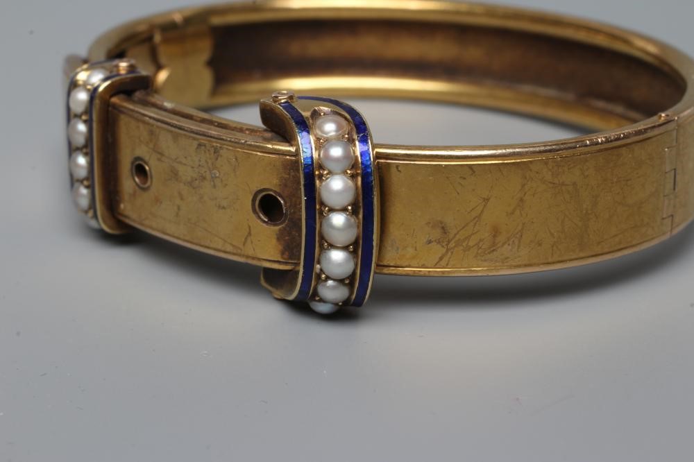 A VICTORIAN STIFF HINGED BUCKLE BANGLE, the upper section with two seed pearl and blue enamel Image