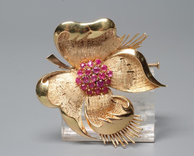A COCKTAIL BROOCH, the large four petalled flowerhead with numerous small rubies claw set to the Image