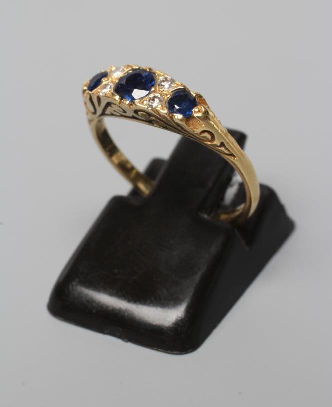 A SEVEN STONE SAPPHIRE AND DIAMOND RING, with carved scroll shoulders and plain 18ct gold shank, Image