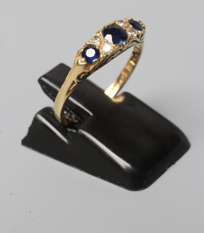 A SEVEN STONE SAPPHIRE AND DIAMOND RING, with carved scroll shoulders and plain 18ct gold shank, Image