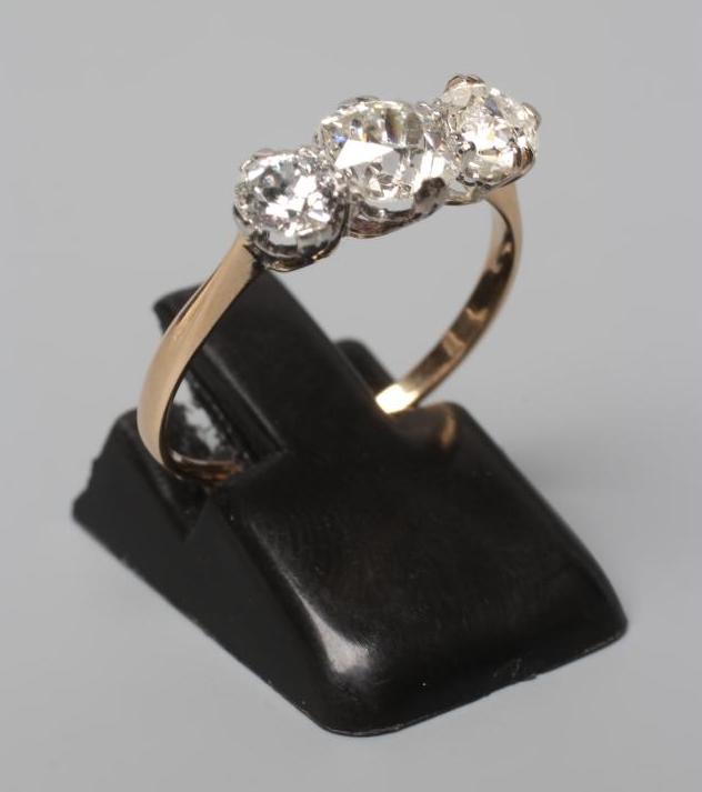 A THREE STONE DIAMOND RING, the old cut stones totalling approximately 1ct, claw set to a plain Image