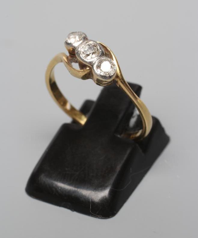 A THREE STONE DIAMOND CROSSOVER RING, the brilliants in rub-over settings to a plain shank stamped Image