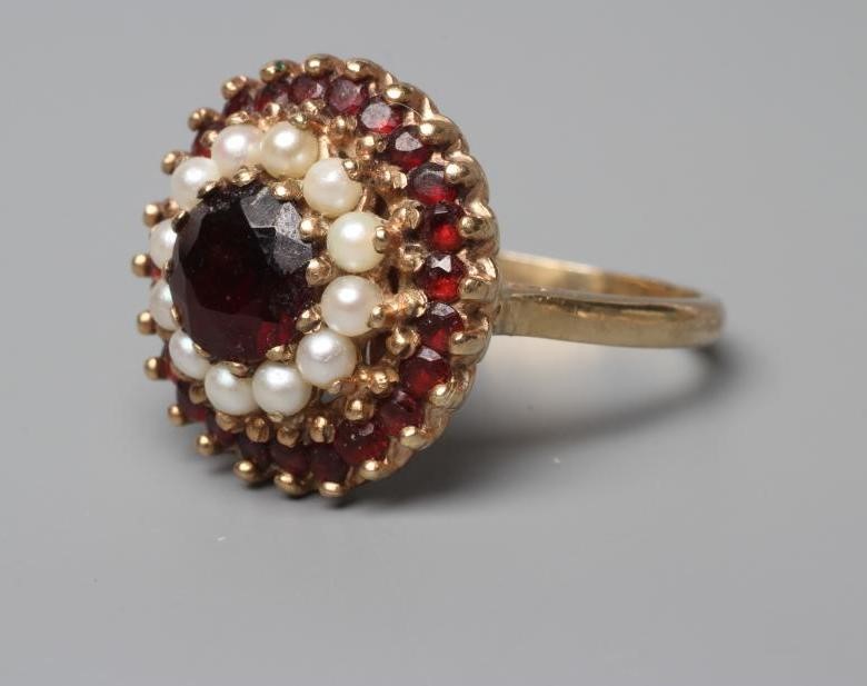 A GARNET AND SEED PEARL CLUSTER RING, point and claw set to a plain shank stamped 9ct, size R (Est. Image