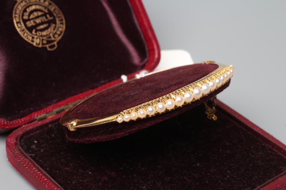 AN EDWARDIAN STIFF HINGED BANGLE, the upper section with nineteen graduated pearls to a plain, Image