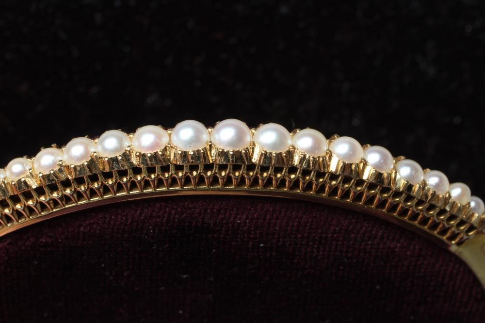 AN EDWARDIAN STIFF HINGED BANGLE, the upper section with nineteen graduated pearls to a plain, Image