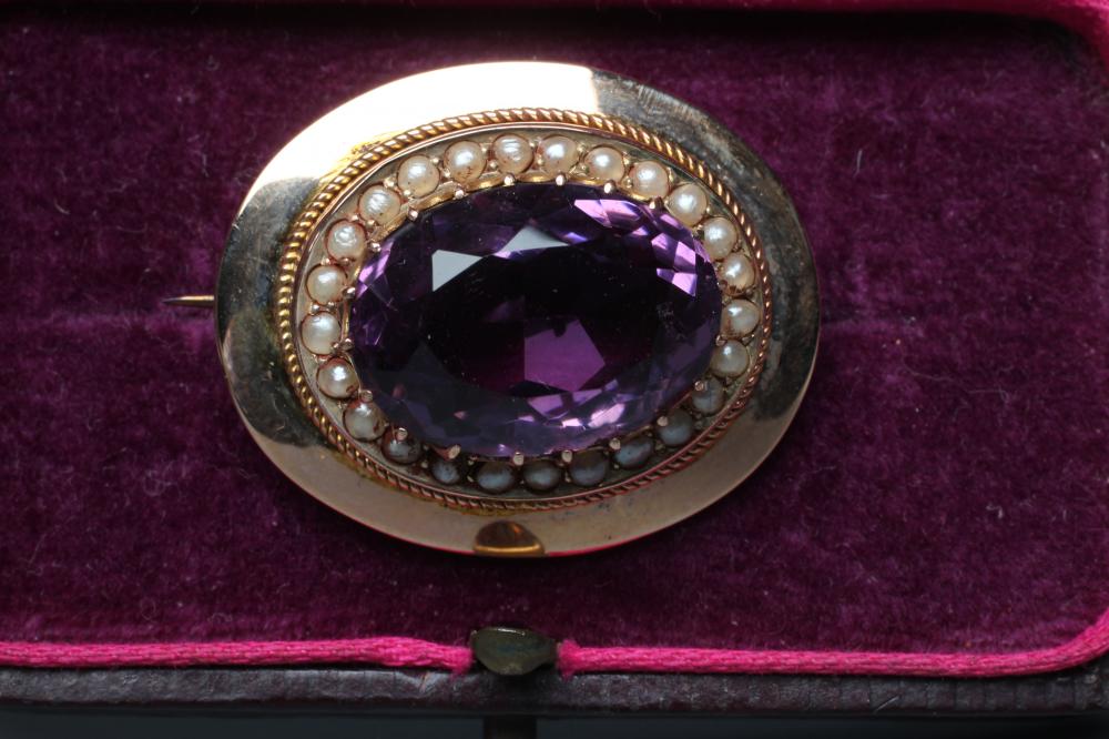 A LATE VICTORIAN AMETHYST BROOCH, the oval facet cut stone set to a border of seed pearls in a plain Image