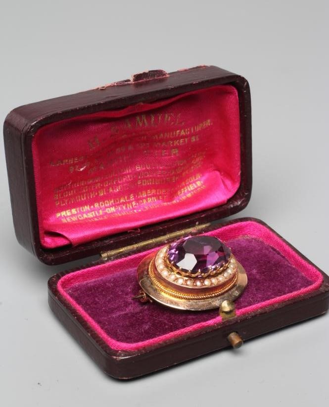 A LATE VICTORIAN AMETHYST BROOCH, the oval facet cut stone set to a border of seed pearls in a plain Image