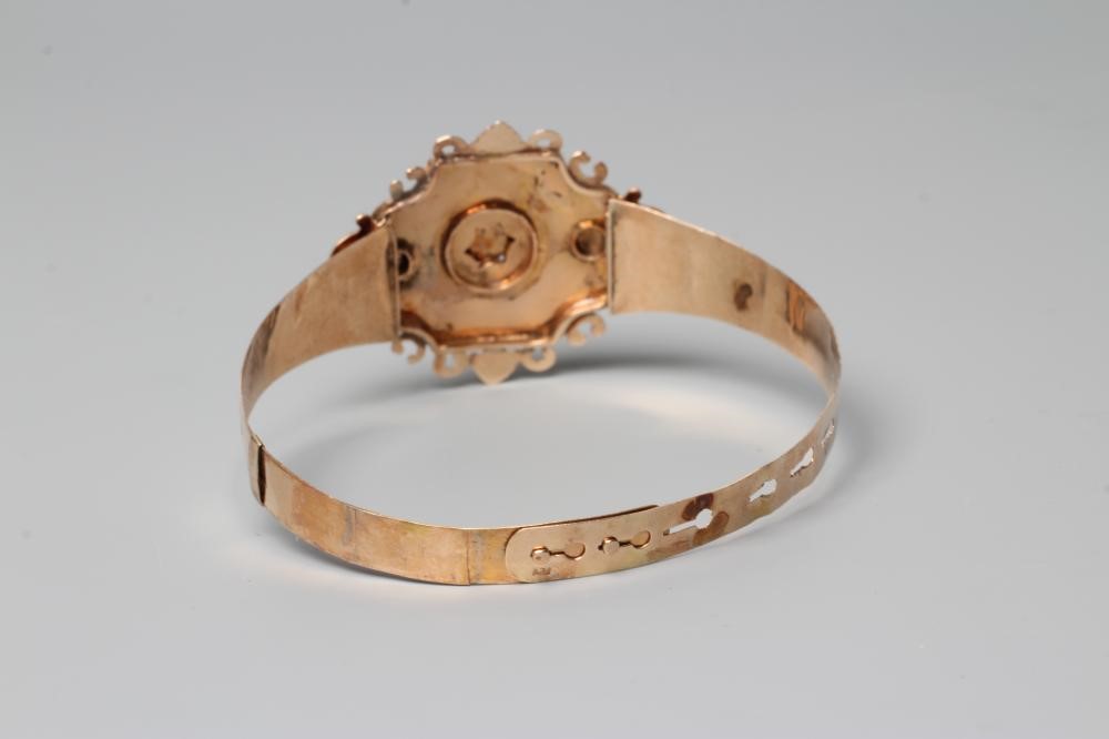 A MID 19TH CENTURY "BUCKLE" BANGLE, the upper section centred by a quatrefoil panel with garnet and Image