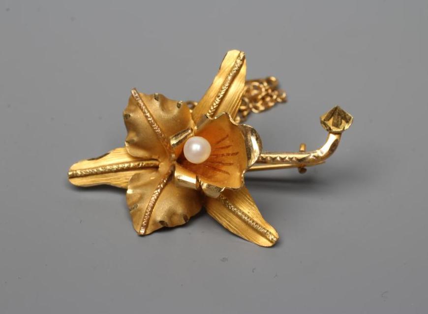 A VENEZUALAN LILY BROOCH centred by a peg set cultured pearl, with safety chain, stamped 18k (Est. Image