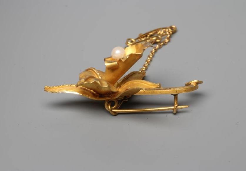A VENEZUALAN LILY BROOCH centred by a peg set cultured pearl, with safety chain, stamped 18k (Est. Image
