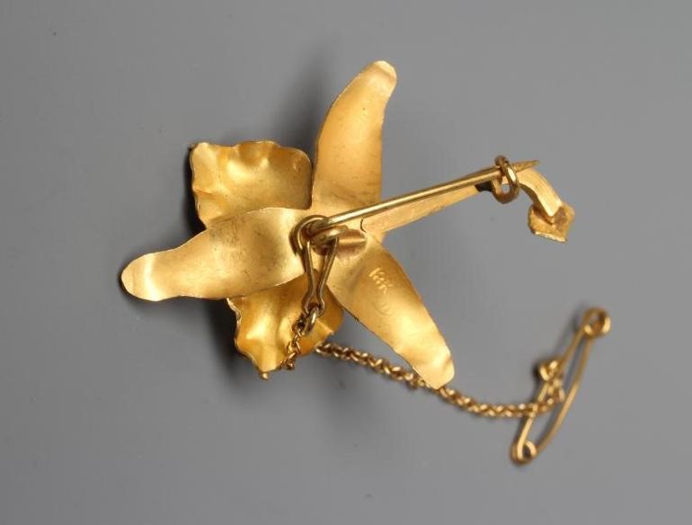 A VENEZUALAN LILY BROOCH centred by a peg set cultured pearl, with safety chain, stamped 18k (Est. Image