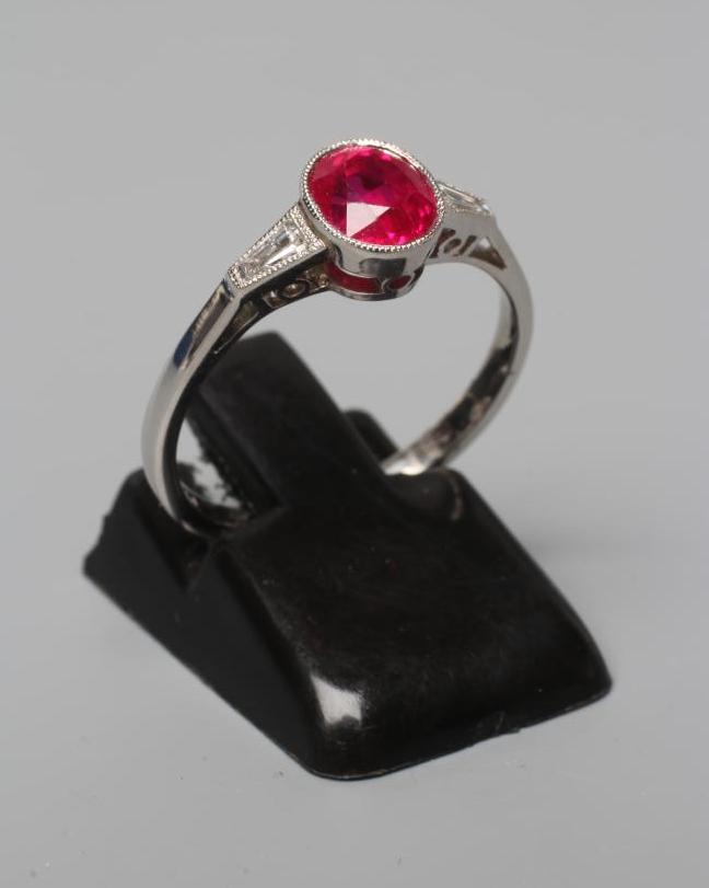 A RUBY RING, the oval facet cut stone of 1.27cts, collet set to shaped shoulders each set with a Image