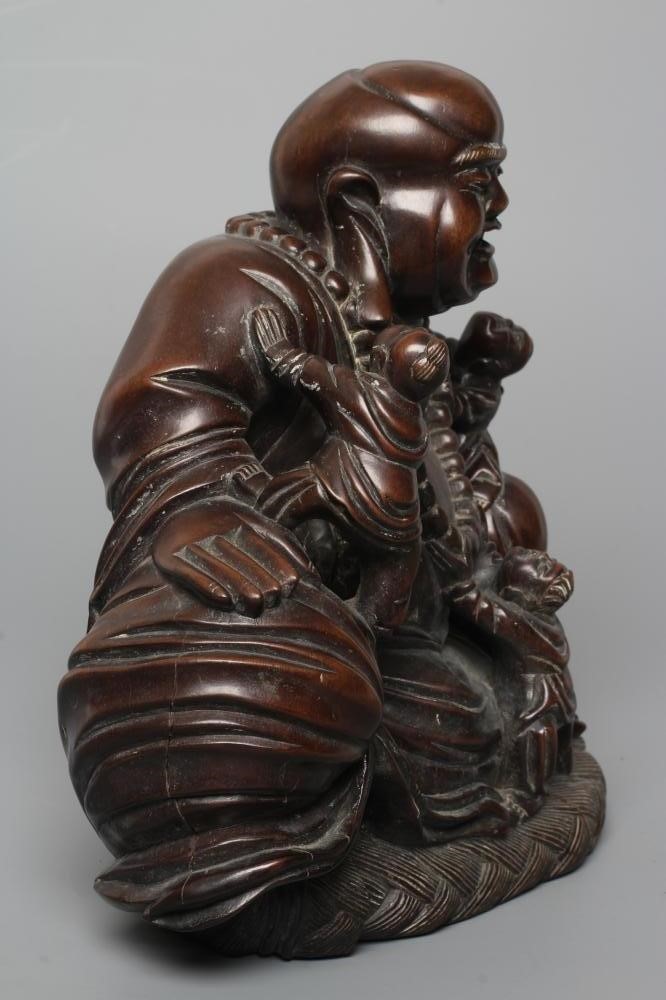 A CHINESE CARVED HARDWOOD BUDDAH, seated wearing a long bead necklace and with three children in Image