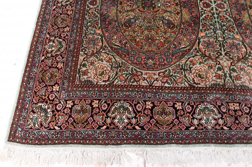 A PERSIAN SILK RUG, the pale green floral field with four oval guls with exotic birds, within an Image