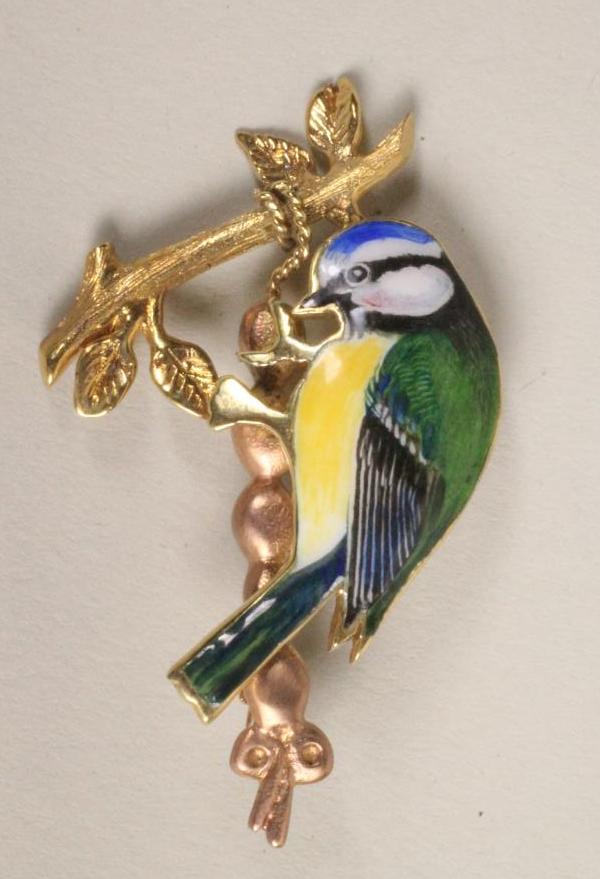 A 9CT GOLD AND COLOURED ENAMEL BROOCH modelled as a bluetit perched upon a leafy branch Image