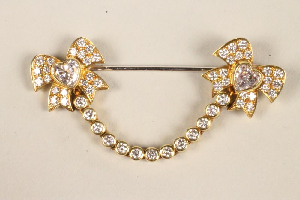 A DIAMOND "SWAG" BROOCH with two ribbon bows centred by a heart shaped stone and tied by a swag of Image